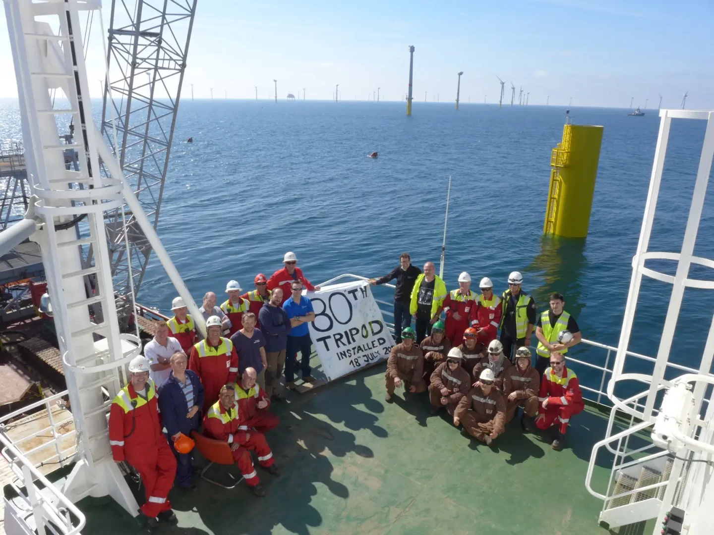 Gruppenfoto von Offshore-Arbeitern und Ingenieuren auf einem Schiff. Die Crew feiert die Installation des 80. Tripod-Fundaments für den Windpark Global Tech I.