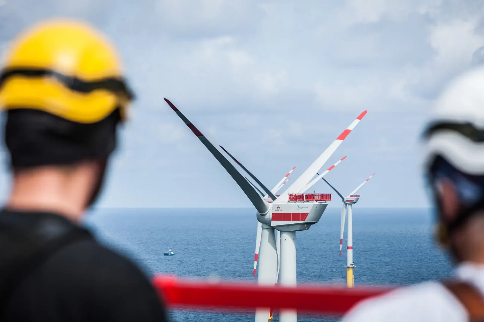 Offshoretechniker von hinten, der oben auf einer Anlage aufs Meer schaut. Im Hintergrund sind weitere Offshore-Windkraftanlagen sichtbar.