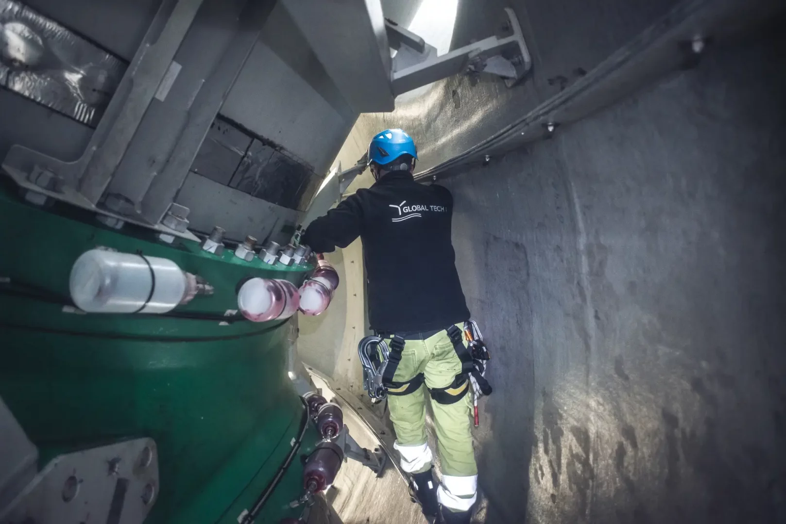 Ein Offshore-Techniker mit Helm und Kletterausrüstung arbeitet im Inneren einer Windkraftanlage von Global Tech I. Sichtbar sind große Maschinenteile.